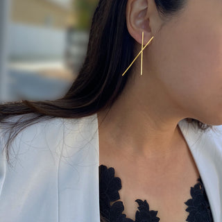 Close-up of a person wearing a stylish pair of Chopstick Earrings by Sonia Hou Jewelry. They are dressed in a black lace top layered with a white blazer. The background is blurred, highlighting the earrings and clothing, evoking the elegance often seen during Lunar New Year celebrations.
