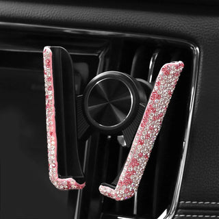 Introducing the Gabba Goods Bling Hands-Free Car Vent Mount: A stylish car phone holder that attaches to your vehicle's air vent. Adorned with sparkly pink crystals, it adds a touch of glamour while ensuring safety and convenience with its hands-free operation. The predominantly black design provides a sleek contrast to the shiny embellishments.