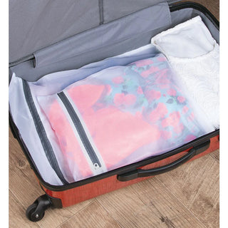 An open red suitcase lies on a wooden floor. Inside, clothes are neatly packed, including a floral garment in an M Design Laundry & Travel Storage Zipper Bag (3-Pack) for delicate protection and a white lacy item. The suitcase features a grey interior.