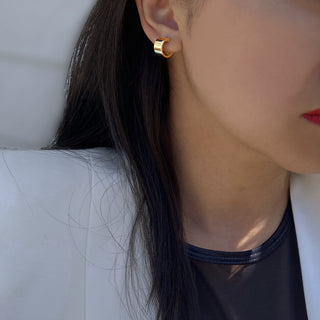 Close-up of a person with long, dark hair wearing Sonia Hou Jewelry's Boss Chubby Mini Hoops Earrings. The person is dressed in a white blazer over a black top, exuding a confident aura. Their skin is partially visible near the neck and face. The background is blurred, emphasizing the earrings and parts of the person’s attire.