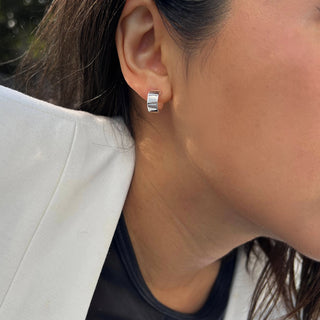 Close-up of a person wearing a white blazer and Sonia Hou Jewelry's Boss Chubby Mini Hoops Earrings. The person is shown from the side, focusing on the confident elegance of the earrings and the ear, with strands of dark hair visible. The background is blurred, placing emphasis on the shimmering Boss Chubby Mini Hoops Earrings.