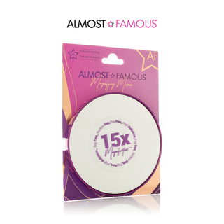 Packaging of the Almost Famous 15X Vanity Mirror with Suction Lock (2-Pack) in Tyrian Purple. The round mirror, equipped with ultra-hold suction cups, is encased in a purple and pink box featuring the Almost Famous branding and a star logo at the top right. The packaging highlights its precise 15x magnification for impeccable detail.