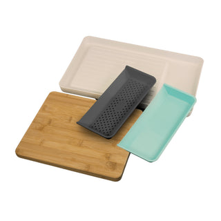 An assortment of kitchen accessories from the Madison York Mess-Free "Cut & Carry" Kitchen Prep Station, including a beige rectangular tray, a wooden cutting board with trays, a black grater with holes, and a blue slotted tray are visibly arranged. The items overlap each other neatly for a tidy and efficient workspace.