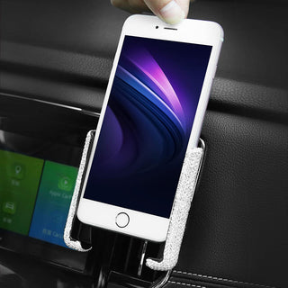 A hand placing a smartphone with a glowing purple and blue screen into a glittery Bling Hands-Free Car Vent Mount by Gabba Goods, attached to the car dashboard. The dashboard display on the left shows a screen with green and blue icons, allowing for seamless, hands-free operation.