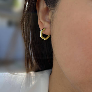 Close-up of a person's ear wearing the Innovate Hexagon Mini Hoop Earrings by Sonia Hou Jewelry. The earrings showcase a sleek, modern style with clean lines and a shiny finish. Part of the person's hair is visible, as well as the collar of a light-colored garment.
