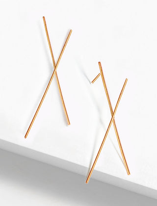 The Chopstick Earrings by Sonia Hou Jewelry feature a minimalist, asymmetrical design of thin gold rods overlapping each other, evoking the elegance of chopsticks. They are elegantly presented against a simple, white background.