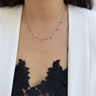 A close-up of a person wearing the Minimalist Rice Bead Chain Necklace by Sonia Hou Jewelry, featuring delicate drop-shaped pendants that symbolize wealth. They are dressed in a black lace top adorned with intricate floral patterns, layered under a chic white blazer.